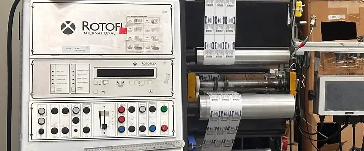 Printed labels running over the rollers of our label slitter in Colmar, beside its control panel